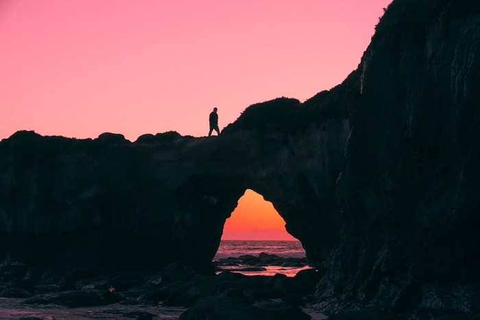 Silhouette of a person walking on a cliff overlooking the ocean at sunset