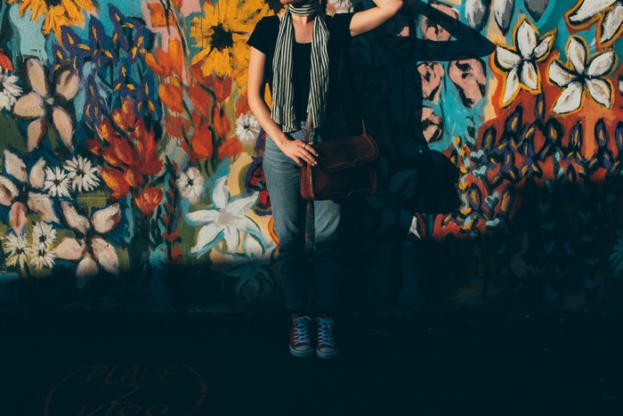 Woman in denim with a bag in front of a colorful mural