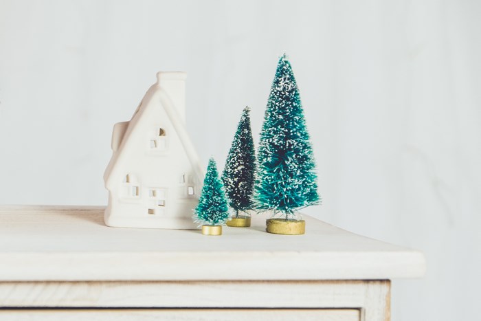 White ceramic house and miniature Christmas trees on a shelf