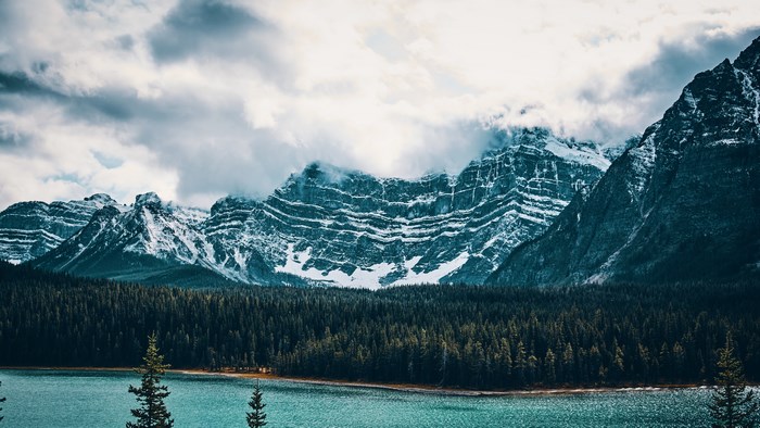 Snow-capped mountains over a teal lake and forest