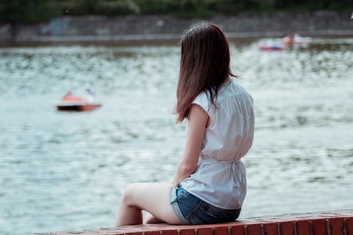 Woman sitting by a lake with boats