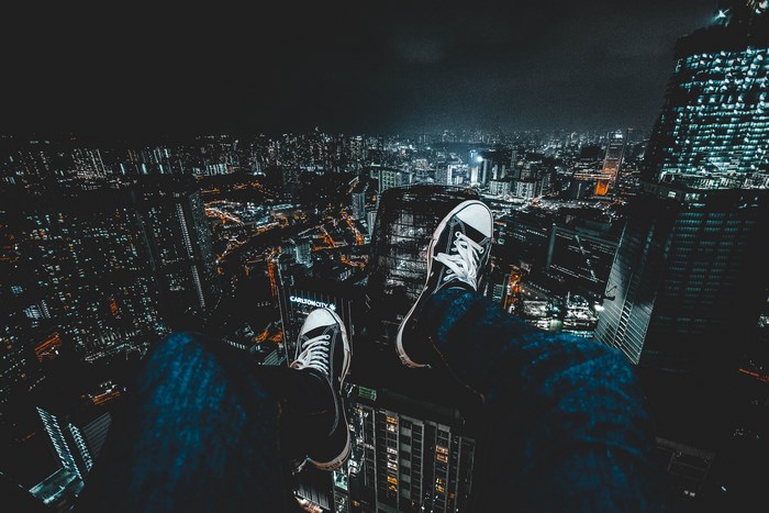 Person sitting on a skyscraper overlooking a city at night