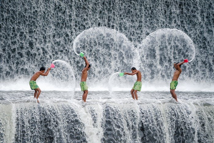 Four men splashing water from buckets at a waterfall in Bali