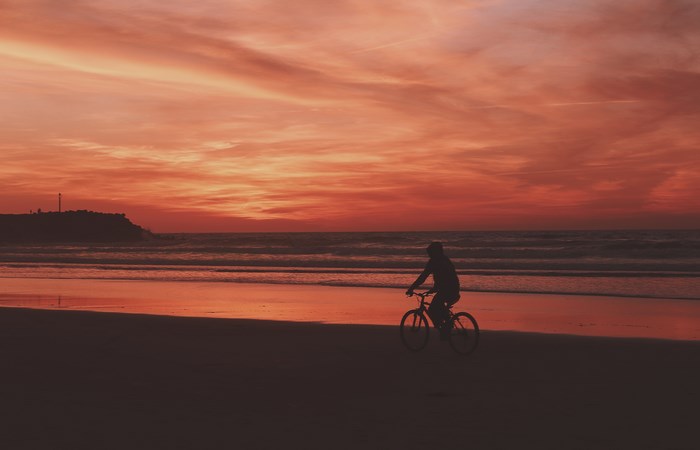 Silhouette of a person riding a bicycle on a beach at sunset