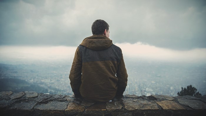 Man in Hooded Jacket Sitting on Stone Wall Overlooking City
