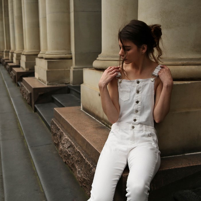 Girl in white overalls sitting by columns