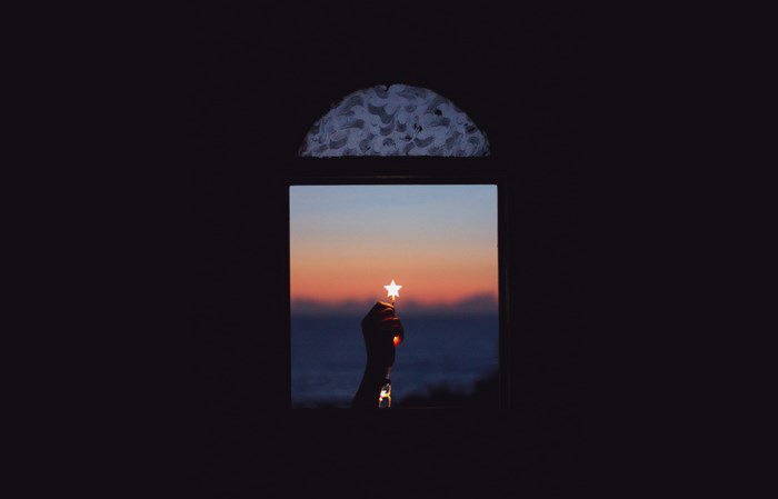 Hand holding a star through a window at sunset
