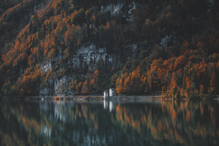 White house on a lake shore with autumn forest and cliff