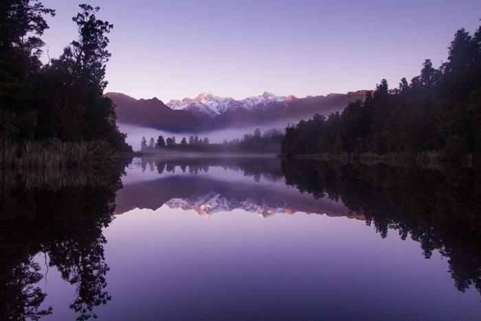 Lake Matheson at sunrise with snow-capped mountains and reflection