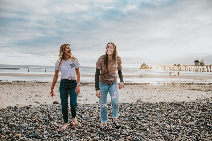 Two young women laughing on a beach with a pier