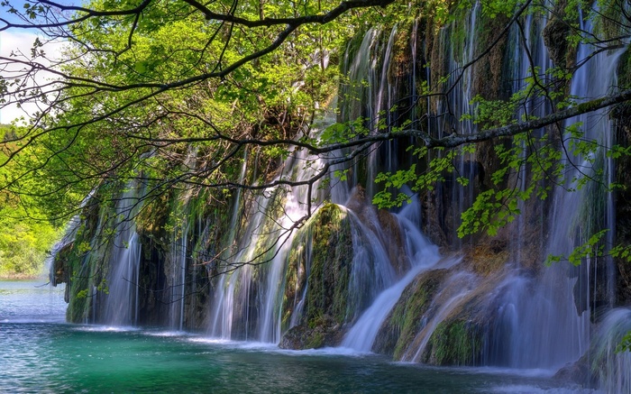Waterfall cascading into a turquoise lake surrounded by greenery