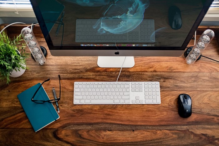 Desk with iMac, keyboard, mouse, notebook, glasses, and plant