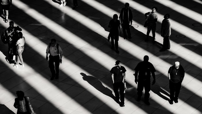 People walking in a sunlit hall with striped shadows