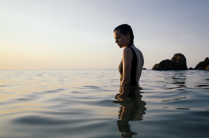 Woman in swimsuit in the ocean at sunset