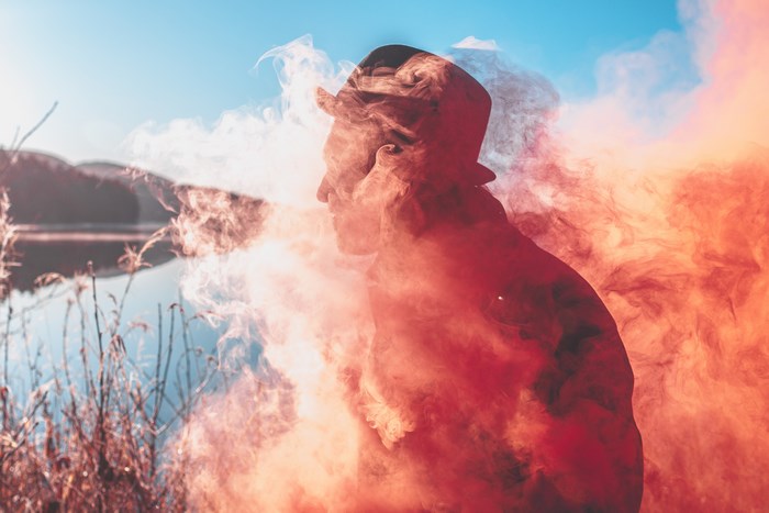 Man in hat with red smoke near lake
