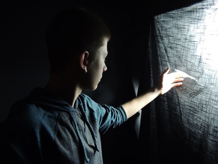 Man touching a torn cloth with light shining through