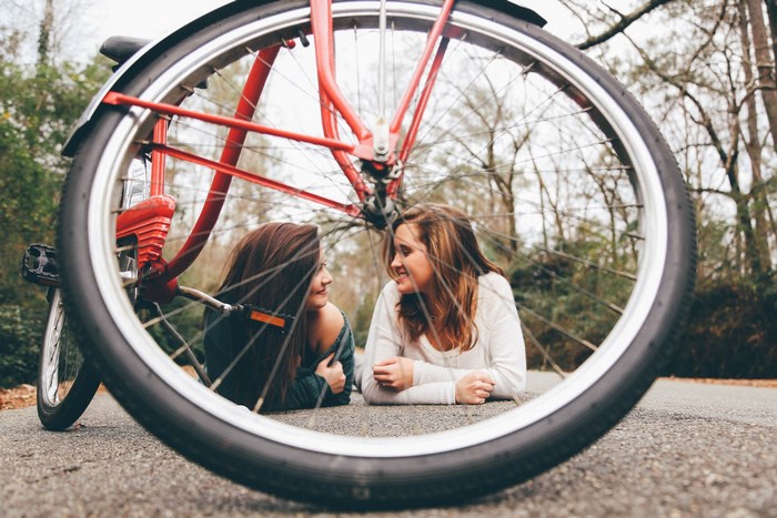 Two women lying on the ground behind a bicycle wheel