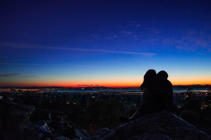 Couple embracing on a hill overlooking a city at dusk