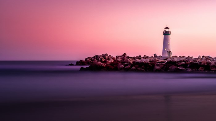 Lighthouse on a rocky shore during pink hour