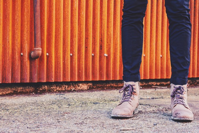 Person wearing jeans and boots standing in front of a rusty wall