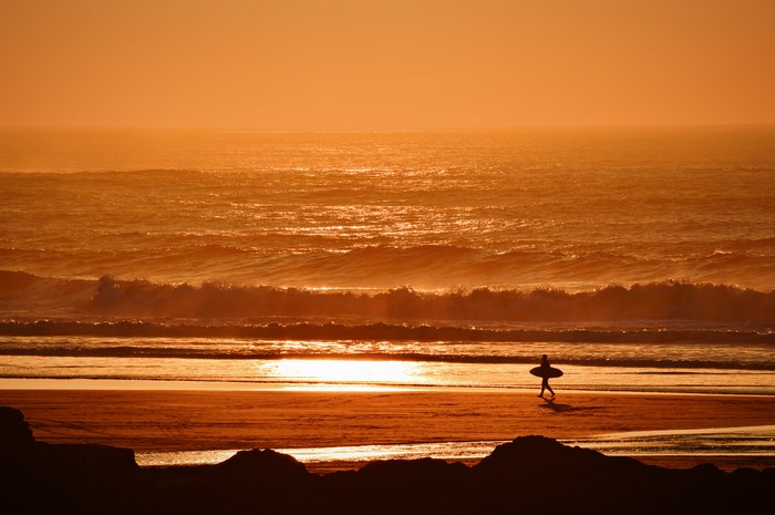 Surfer walking on beach at sunset in Cornwall