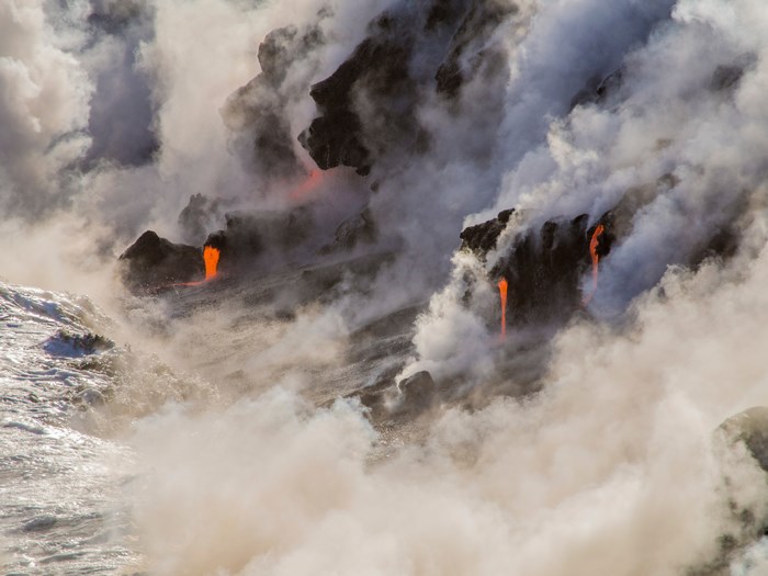 Lava flows into the ocean with steam and smoke
