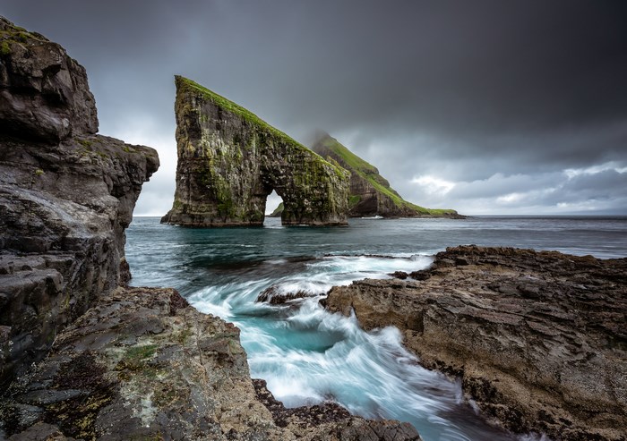 Sea stack with arch in the ocean under stormy clouds