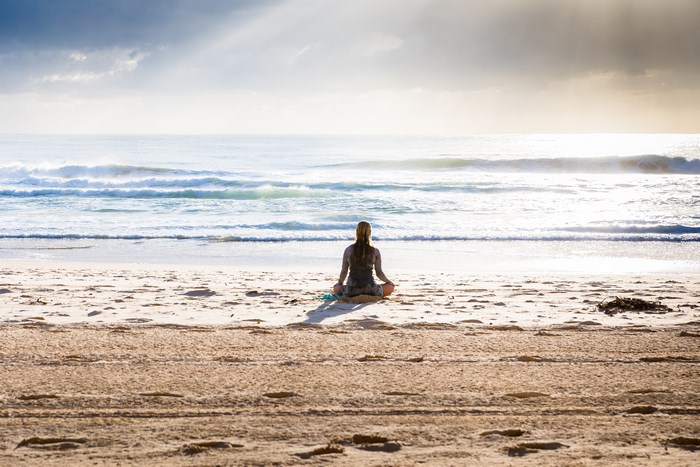 Woman Meditating on Sandy Shore at Sunrise