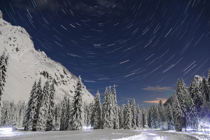 Star trails over a snowy mountain forest at night
