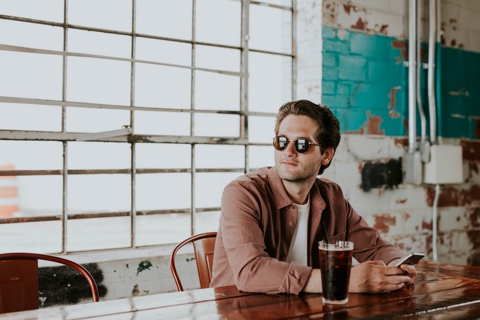 Man with sunglasses using phone at table with drink