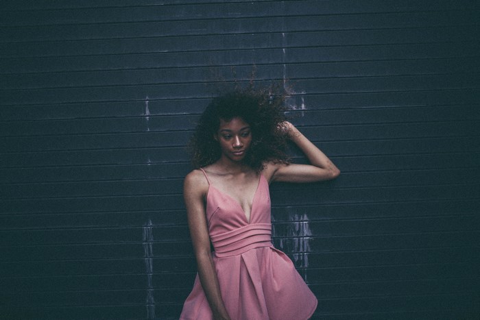 Woman in pink dress leaning against a dark wall