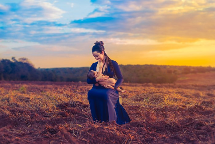 Mother breastfeeding baby in a field at sunset