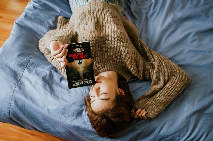Woman in sweater reading a book on a bed