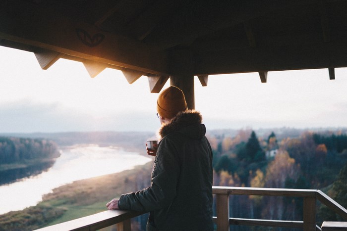 Person holding a cup on a balcony overlooking a river in autumn