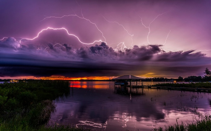 Lightning storm over a lake at sunset with a boathouse