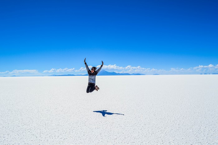 Woman jumping on a white salt flat under a blue sky