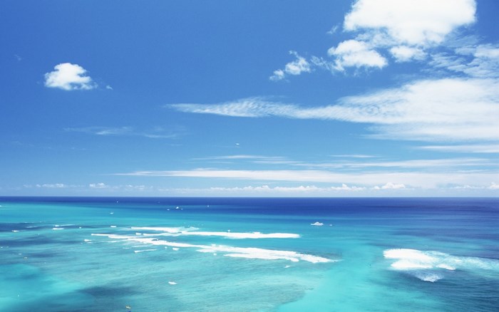 Turquoise ocean with white waves under a blue sky with clouds
