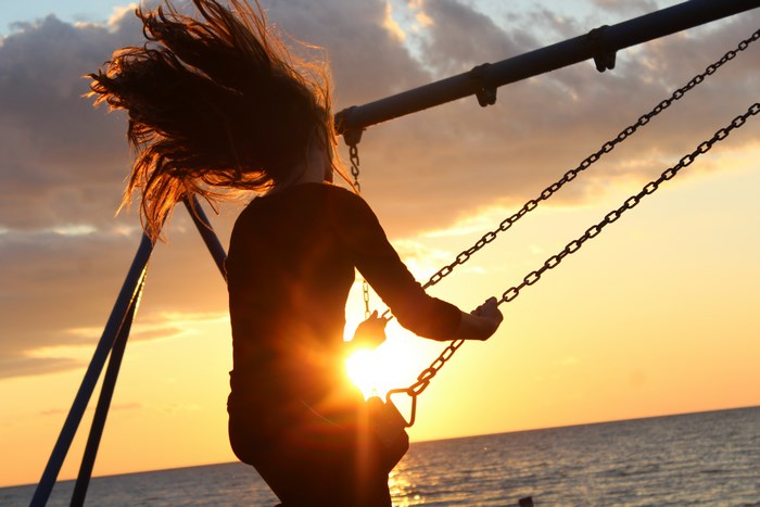Girl on a swing at sunset over the ocean