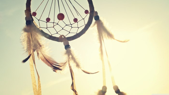 Dreamcatcher with feathers against a bright sky