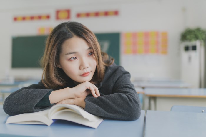 Asian student girl resting her head on a book in a classroom