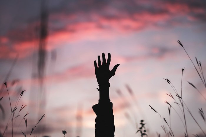 Silhouette of a hand raised against a sunset sky