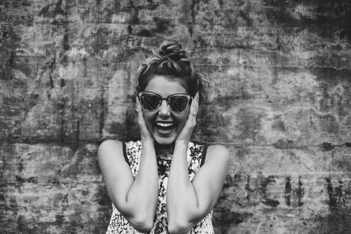 Woman in sunglasses laughing against a textured wall