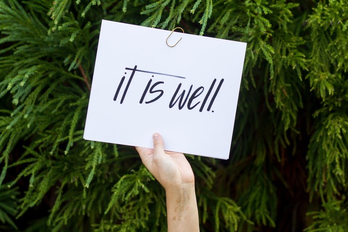 Hand holding a sign with "it is well" written on it