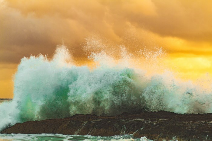 Crashing ocean wave against rocky shore at sunset