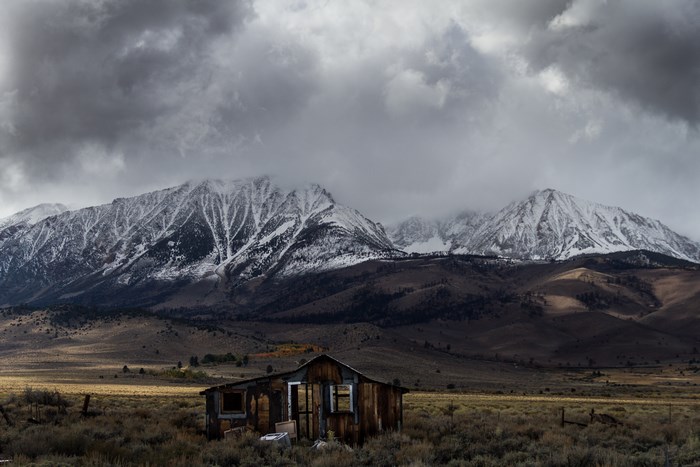 Abandoned shack in front of snow-capped Sierra mountains under stormy clouds
