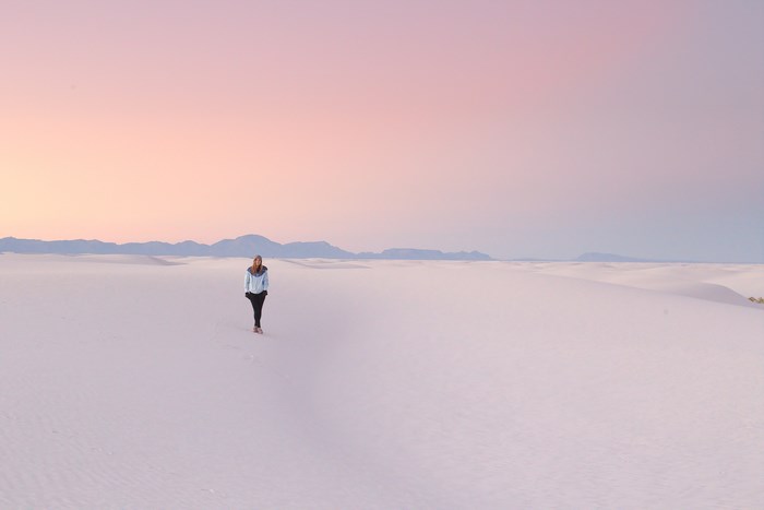 Woman walking in white sand dunes at sunset