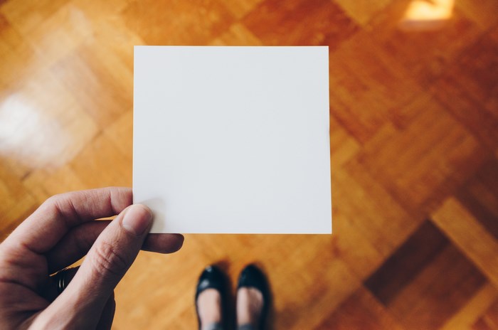 Hand holding a blank white card over a wooden floor