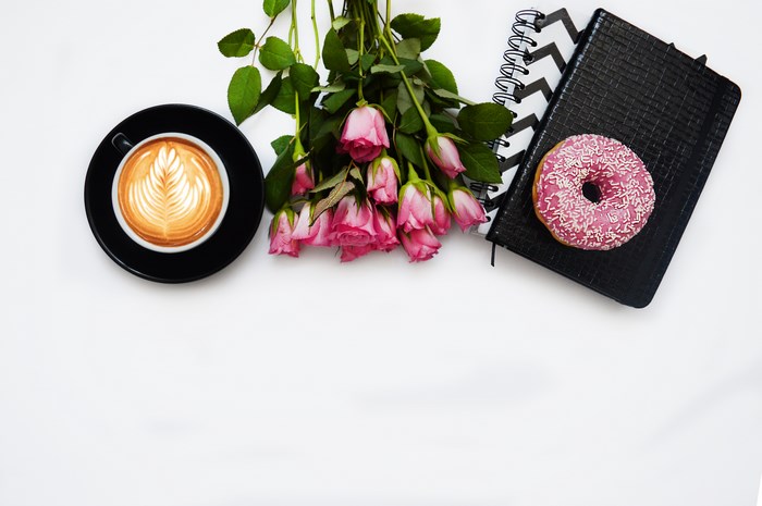 Flatlay of coffee, pink roses, donut, and notebooks