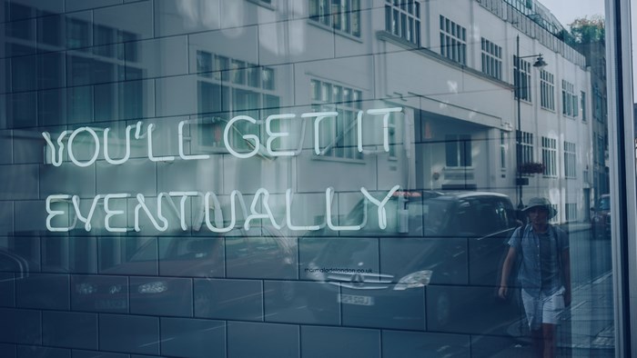Neon sign "You'll Get It Eventually" reflected in a window