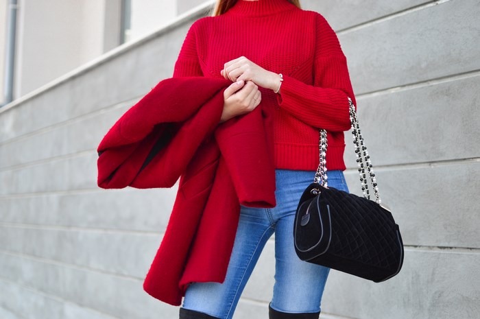 Woman in red sweater and jeans holding a red coat and black bag